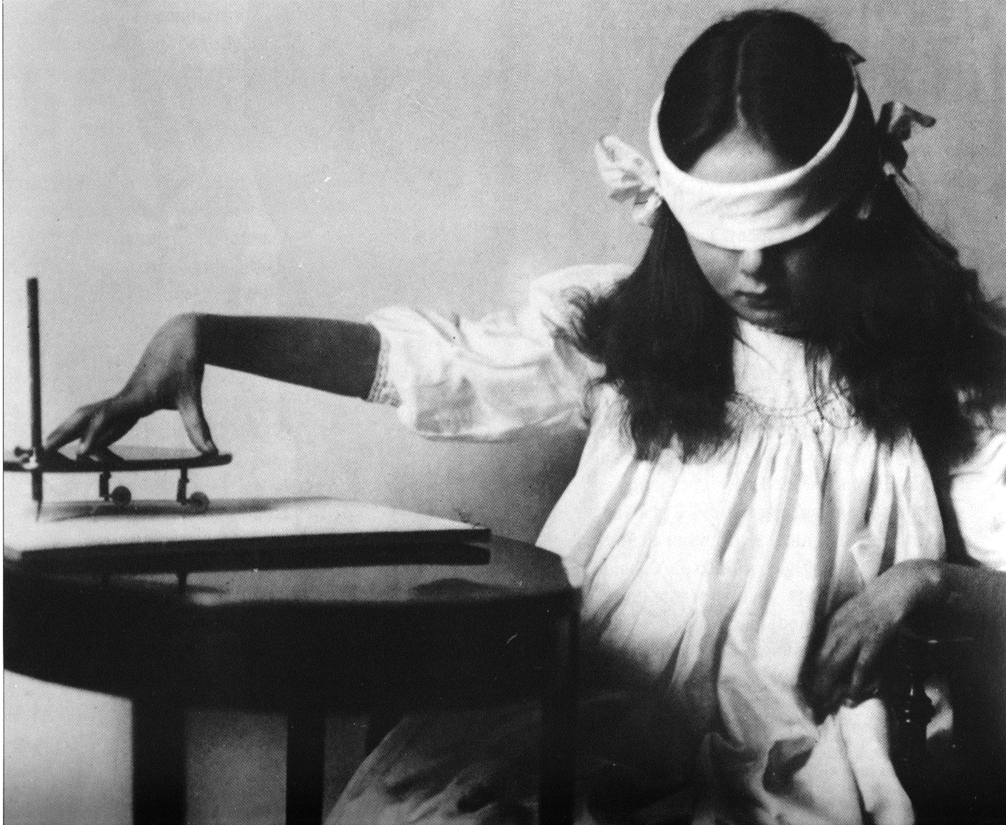 Fotografia de médium com os olhos vendados escrevendo em uma mesa, demonstrando a independência da escrita psicográfica em relação à visão física.